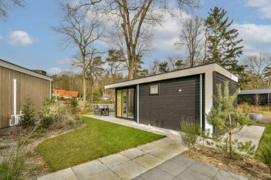 Bahçenin ortasında bir ev. Evin her iki tarafında da ağaçlar ve çalılar var. Açık teras alanı var.