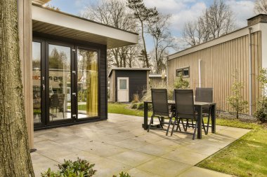 Bahçenin ortasında, yaprakları olmayan büyük bir ağacın yanında, sandalyeleri ve masaları olan bir teras.