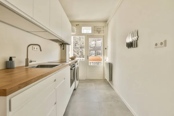 床に白いキャビネットと木製のカウンターの上に長い狭いキッチンとバルコニーにつながるオープンドア — ストック写真
