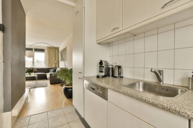 Lavabo, bulaşık makinesi ve kahve makinesi için beyaz dolapları olan bir mutfak.
