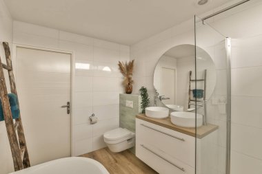 Modern bir banyo. Ahşap döşemeleri ve duvarlarında beyaz fayanslar var. Küvetin üzerinde de büyük bir ayna var.