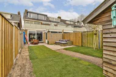 Bahçesinde ahşap çitler ve yeşil çimenler olan bir bahçe alanı evin yan tarafında ahşap kaplamalarla çevrilidir.