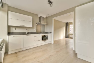 Odanın ortasında beyaz dolapları ve ahşap döşemeleri olan bir mutfak var.