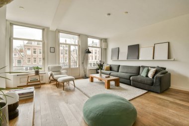 Ahşap döşemeli ve geniş pencereli bir oturma odası apartmanın önündeki sokağa bakıyor.