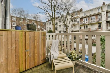 Arka bahçesinde sandalyeler ve ağaçlar olan bir balkon güneşli bir günde bir apartmana bakıyor.