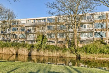 Nehrin karşısından diğer binalara götürülen ağaçların ve çalıların olduğu bir apartman kompleksi.