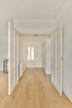 Beyaz duvarları ve sağ tarafında ahşap döşemeleri olan boş bir oda. Başka bir odaya açılan bir kapı var.