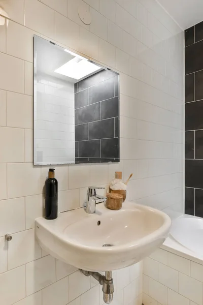 a white sink in a bathroom with black tiles on the wall behind it and a mirror hanging over the sink