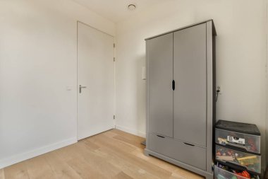 Beyaz duvarları ve ahşap döşemeleri olan boş bir oda odadaki küçük bir depoyu ortaya çıkarmak için açık.