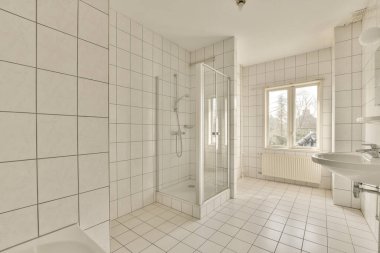 Duvarlarında ve zemininde beyaz fayanslar olan bir banyo ve duş kabininde bir tuvalet lavabonun yanında.