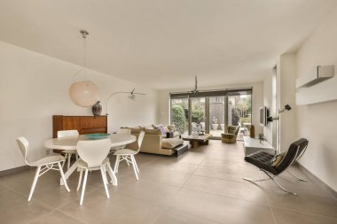 Beyaz mobilyaları ve arka bahçedeki avluya bakan büyük pencereleri olan bir oturma odası.