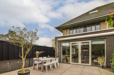 Avlunun ortasında bir masa ve sandalyeler olan bir dış alan, diğer tarafında küçük bir ağaç var.