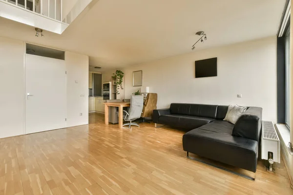 房间中央有木制地板和白色墙壁的客厅是一个黑色皮沙发 — 图库照片