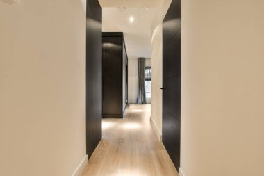 Ahşap döşemeli ve sağ taraftaki evlere açılan siyah kapılı uzun bir koridor.