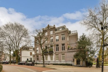 Yolun kenarına park edilmiş ağaçlar ve arabalarla dolu bir caddenin ortasındaki eski bir tuğla bina.