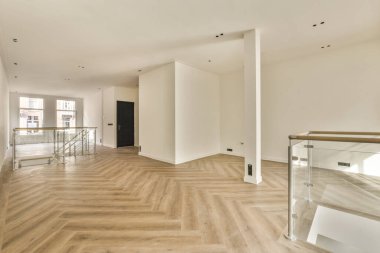 Ahşap döşemeleri ve beyaz duvarları olan boş bir oturma odası var. İkinci kata çıkan bir merdiven var.