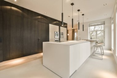 Beyaz tezgahları ve karanlık ahşap dolapları olan modern bir mutfak teneffüs lambasıyla aydınlatılıyor.