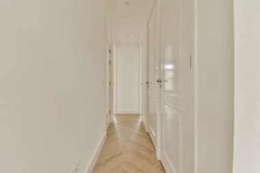 a long hallway with white walls and wood flooring on the right hand side, there is an open door leading to another room