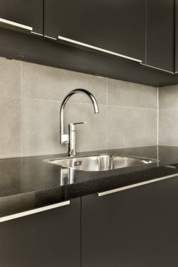 Modern bir mutfak, siyah tezgahlı ve arkasında beyaz fayanslar olan paslanmaz bir lavabo.