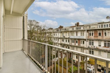 Arka planda bazı binalar ve üzerinde mavi gökyüzü olan bir balkon güneşli bir günde bir apartmandan görüldüğü gibi.