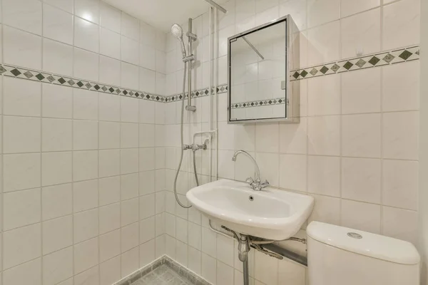 白いタイルと壁に緑のトリムの小さなバスルームシンクの上には鏡がかかっています — ストック写真