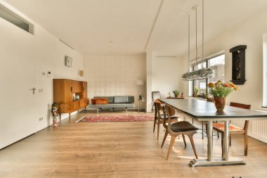 İki kahverengi sandalyeyle çevrili büyük bir yemek masası dahil, ahşap döşemeli ve beyaz duvarlı bir oturma odası.