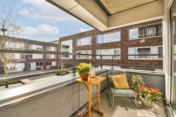 stock image a balcony with some flowers on the table and an orange chair in the fore - eyed view is very sunny