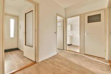 Beyaz duvarları ve sağ tarafında ahşap döşemeleri olan boş bir oda. Köşesinde bir ayna var.