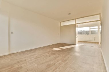 Boş bir oturma odası, ahşap zemin ve şehir manzarasına bakan geniş bir pencere.