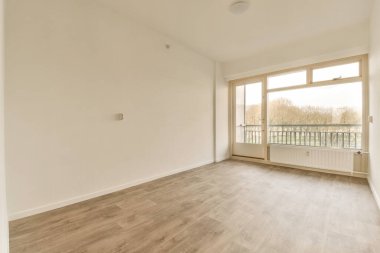 Boş bir oturma odası, ahşap döşeme ve evin önündeki sokağa bakan büyük pencereli.