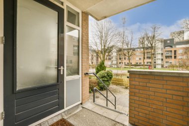 Ön tarafında bir kapı ve tuğla duvar olan bir dış alan. Görüntü içeriden alınıyor, net değil.