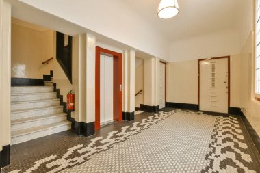 Boş bir oda, fayanslı zemin ve ortasında kırmızı kapı, her iki tarafında beyaz duvarlar, ve kapıların etrafında siyah süslemeler.