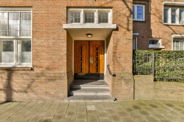 Güneşli bir günde, pencereleri beyaz ve kırmızı kapılı tuğla bir bina.