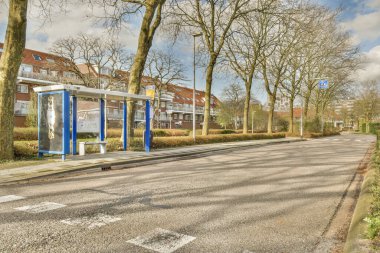 Boş bir caddenin ortasında bir otobüs durağı içinde araba ya da insan yok ve yol boyunca ağaçlar var.