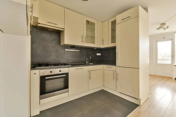 オーブンの前の床に白い食器棚と黒いカウンターがあるキッチンシンクと食器洗い機 — ストック写真