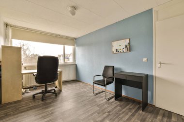 Masası, sandalyesi ve bilgisayarı olan bir oda. Pencereye açılan açık bir kapının önünde.