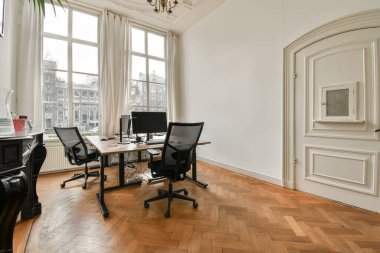 Şehir manzarasına bakan geniş bir pencerenin önünde iki bilgisayar masası olan bir ev ofisi.