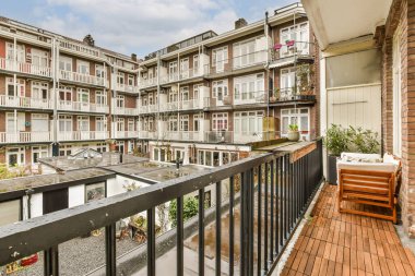 Arka planda bazı binalar olan bir balkon ve balkon alanının sağ tarafında boş bir bank.