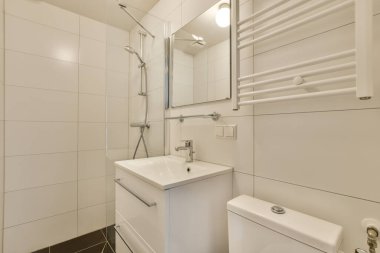 Beyaz duvarlı küçük bir banyo ve yerde siyah fayanslar lavabonun üstünde bir ayna var.