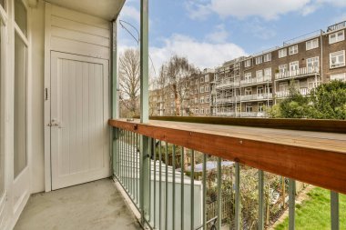 Sağ tarafında açık bir kapı olan bir balkon ve arka tarafında da diğer tarafta binalar.