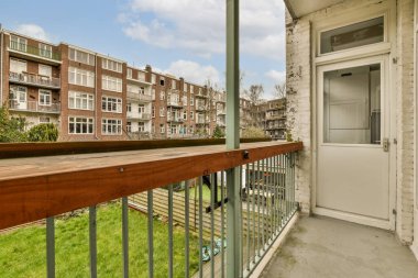 Arka planda bazı binalar olan bir balkon ve kapının yanında yeşil çimenler büyüyen açık beyaz bir kapı var.