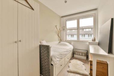 Duvarın köşesinde yatağı, masası ve televizyonu olan küçük bir oda beyaza boyanmış.