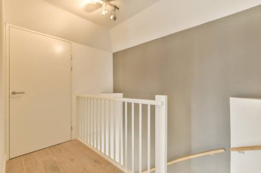 Boş bir oda, ahşap döşemeli ve merdivenlerde beyaz parmaklıklar var. Bu evin ikinci katına çıkıyor.