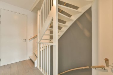 Gri duvarları ve ahşap döşemeleri olan bir evin beyaz merdivenleri tahtadan yapılmıştır.