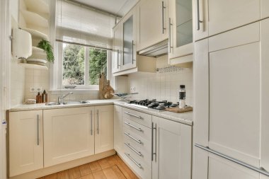 Mutfakta beyaz dolaplar ve aletler tezgahın üstünde lavabonun önünde, penceresi solda.