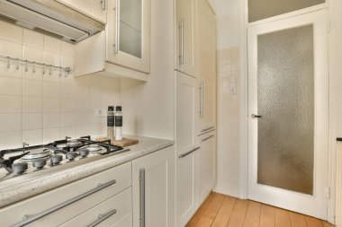 Odanın ortasında beyaz dolapları ve ahşap döşemeleri olan bir mutfak var.