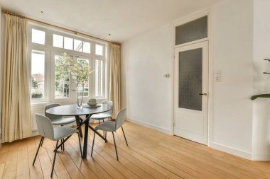 Aşağıdaki sokağa bakan büyük pencereli bir odada bir yemek masası ve sandalyeler var.