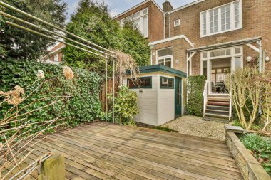 Arka bahçesinde bir kulübe ve tuğla evin önünde ağaçlarla çevrili bitkiler var.