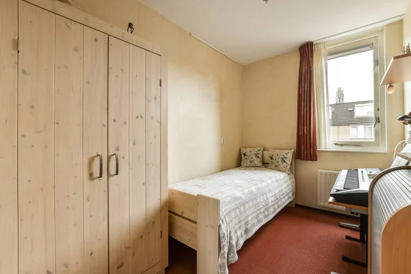 stock image a small room with a bed and cupboards on the left side of the room, there is a window that looks out into