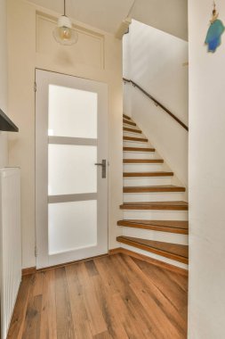 Ahşap döşemesi olan boş bir oda ve çok temiz olan ikinci kata çıkan beyaz bir kapı.